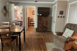 Cozy living room with dining table, armchair, TV on a cabinet, and doorways leading to other rooms.