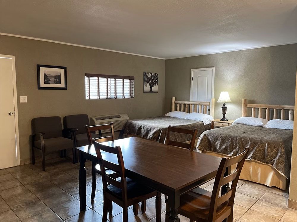 A motel room with two beds, a table with chairs, and two armchairs. Brown walls and furniture.