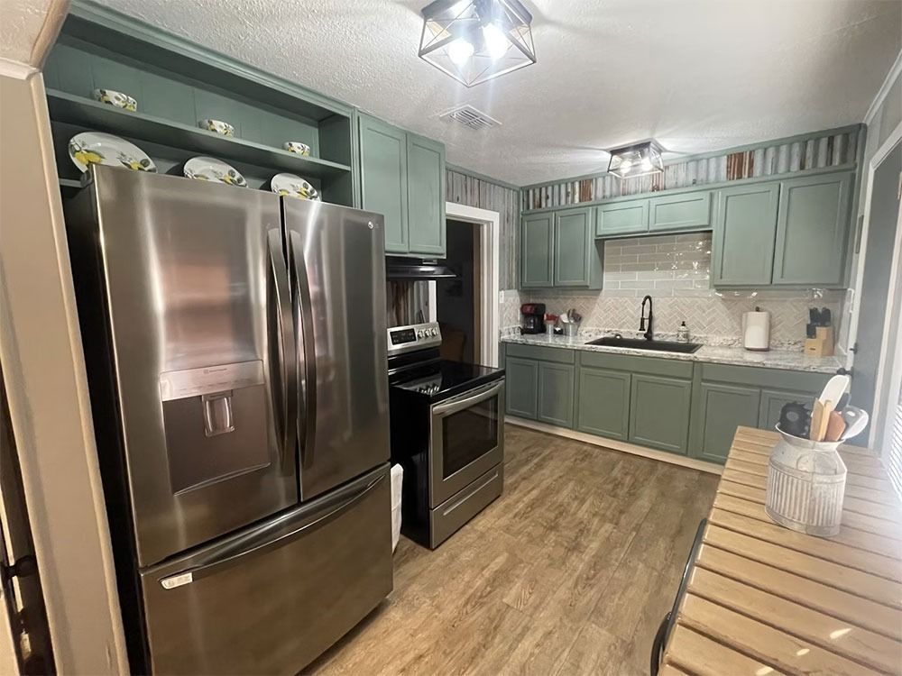 Kitchen with light green cabinets, stainless steel appliances, and light wood-look flooring. The room has a bright, airy feel.