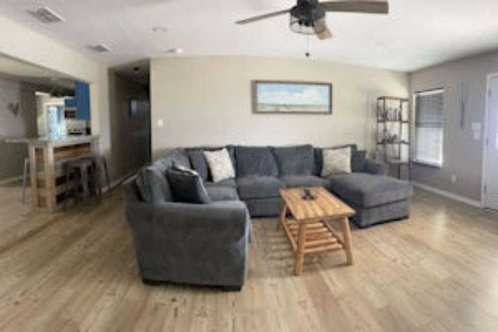 Living room with a gray sectional sofa, wooden coffee table, and a light-colored floor. A bar is in the background.