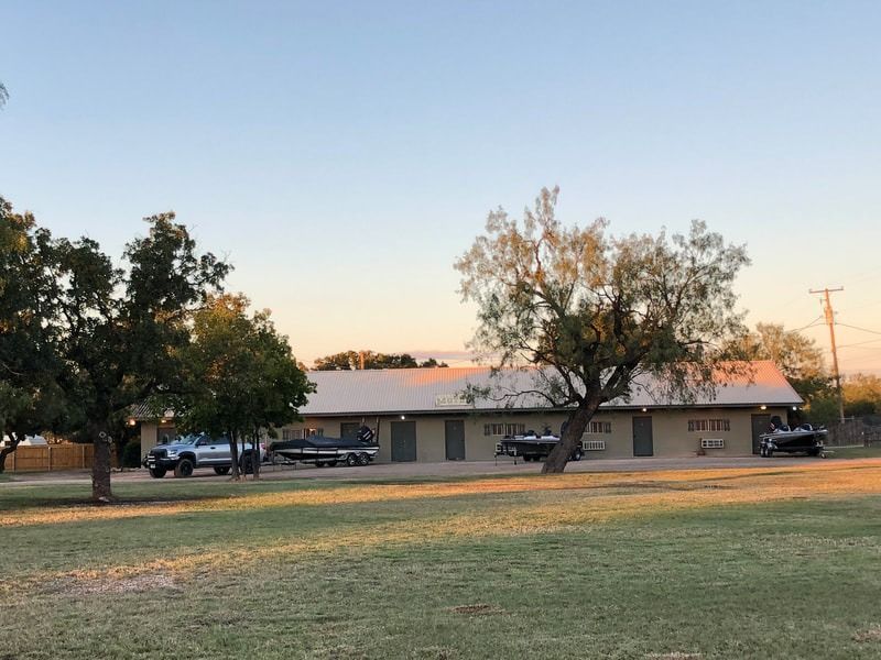 A motel with several rooms, a grassy yard, and trees. Three boats are parked in front of the rooms.