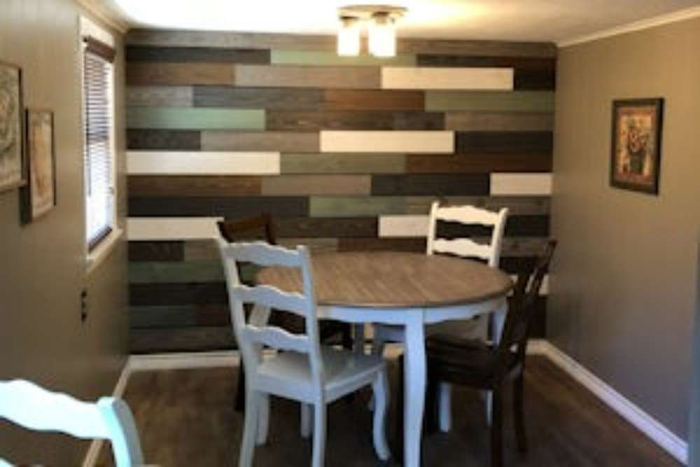 Dining room with a round white table and four chairs, one wood-colored and three white. A multi-colored wood plank accent wall is behind the table.