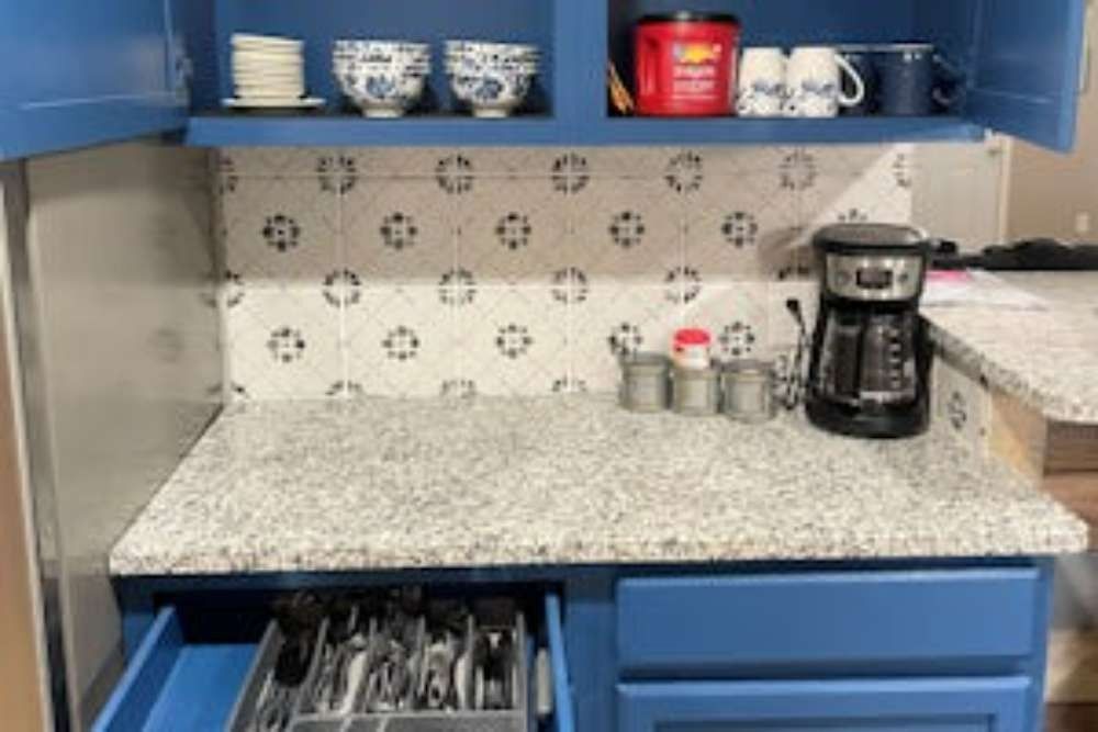 Blue kitchen cabinets with a granite countertop and tiled backsplash. Open drawer reveals silverware.