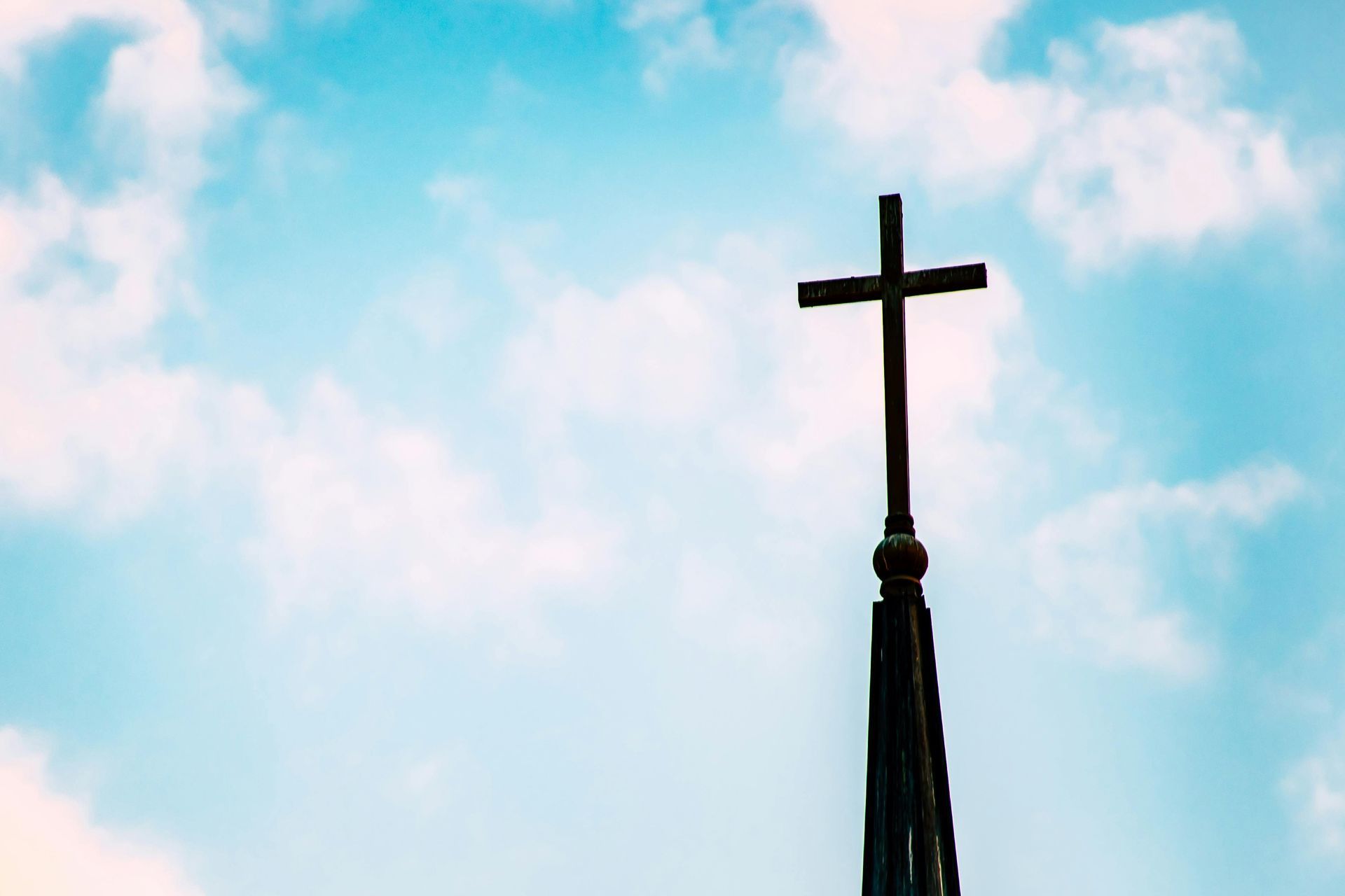 Cross atop a church steeple against a bright blue sky with clouds