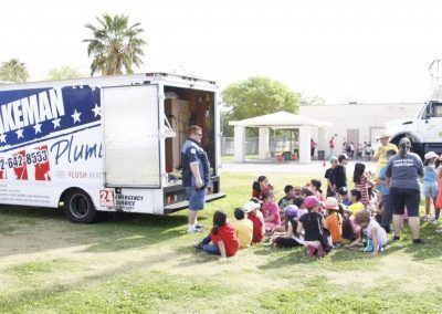 A group of children are sitting in front of a keman plumbing truck.