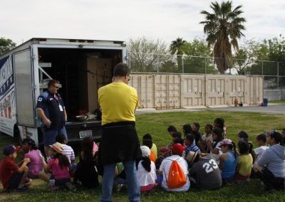 A group of children are sitting on the grass in front of a truck with the number 23 on it