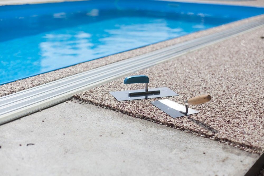 Poolside Construction: Trowels on Gravel Border Next to A Blue Pool — Coastcrete Concrete Specialist in Newcastle, NSW