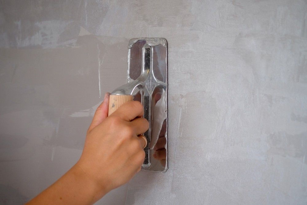 Hand Using a Trowel to Smooth Grey Wall Plaster — Coastcrete Concrete Specialist in Tea Gardens, NSW