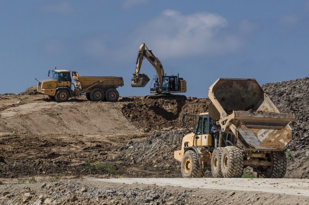 Excavator Loading Dirt Into a Dump Truck on A Construction Site; Blue Sky — Coastcrete Concrete Specialist in Newcastle, NSW