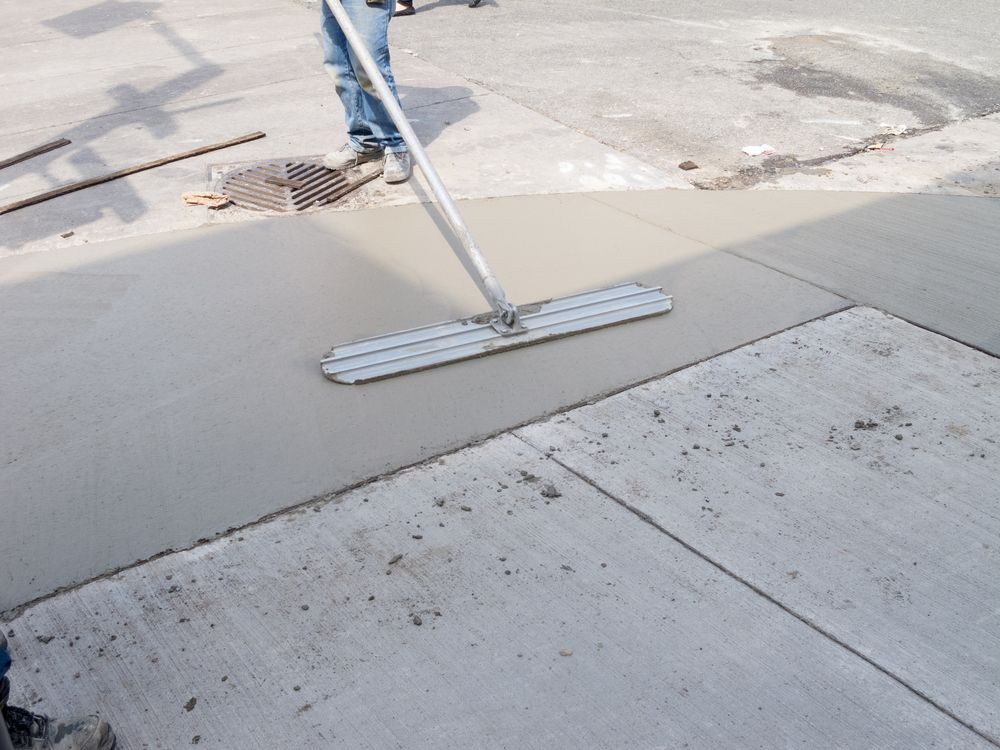 Person smoothing wet concrete with a long-handled float on a city sidewalk.