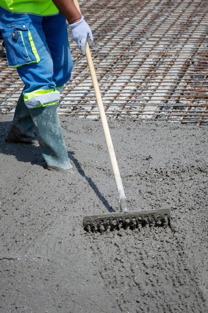 Construction Worker Raking Wet Concrete, Wearing Boots and Safety Gear — Coastcrete Concrete Specialist in Anna Bay, NSW