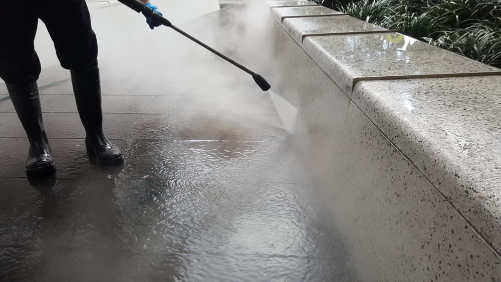 Person Power Washing a Wet Stone Sidewalk with Steam — Coastcrete Concrete Specialist in Taylors Beach, NSW