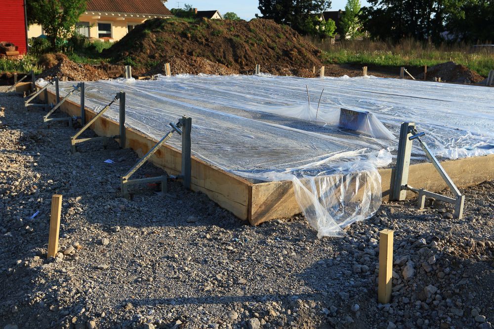 Foundation construction site with wooden frame and plastic covering. Gravel ground.