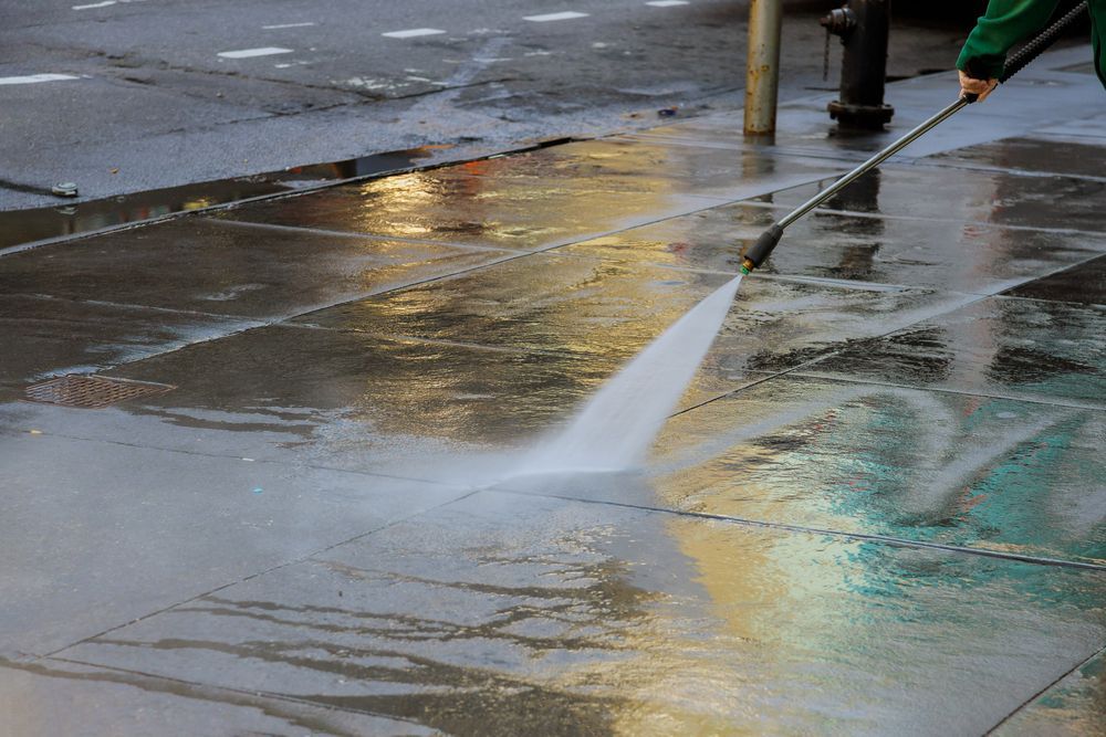 Sidewalk being power washed with water, creating a wet, clean streak on the pavement.
