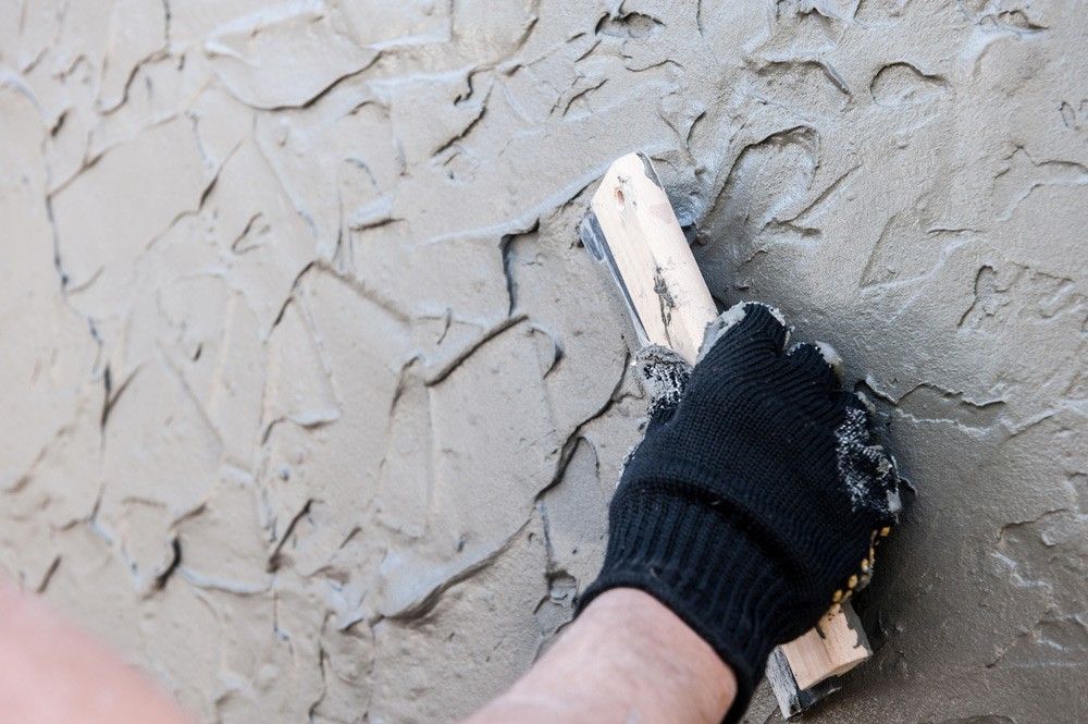 Hand with Black Glove Applying Plaster to A Wall Using a Trowel — Coastcrete Concrete Specialist in Tea Gardens, NSW