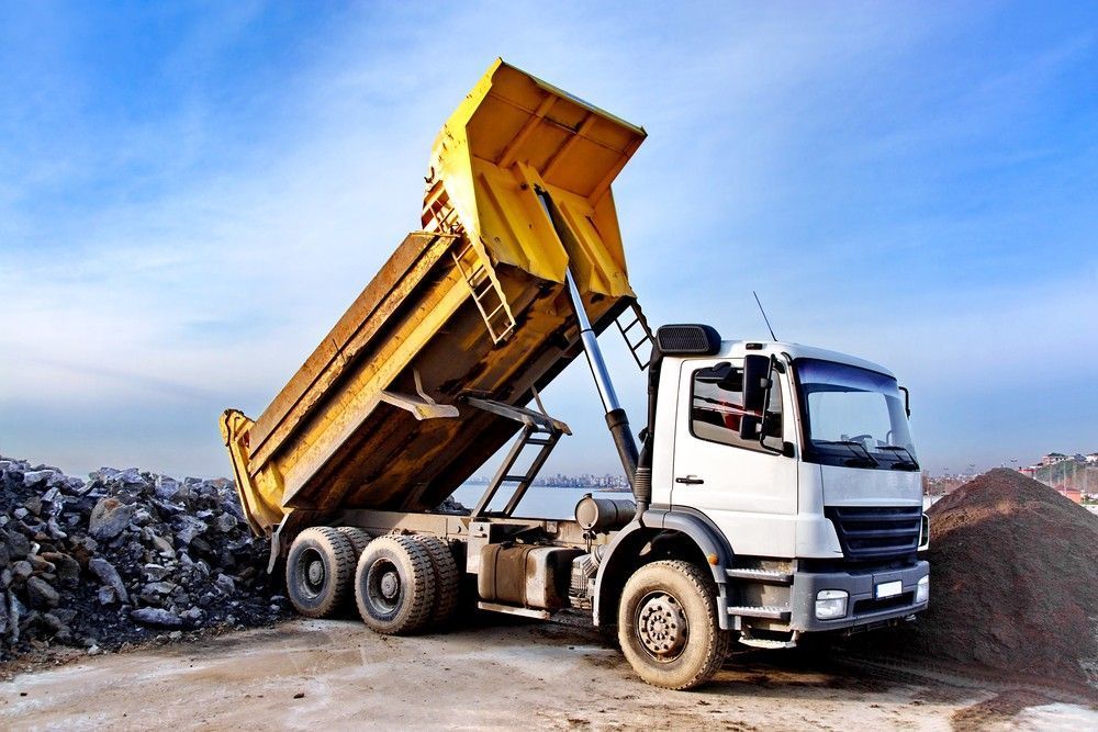 Yellow Dump Truck Dumping Load of Gravel, Blue Sky Backdrop — Coastcrete Concrete Specialist in Tea Gardens, NSW