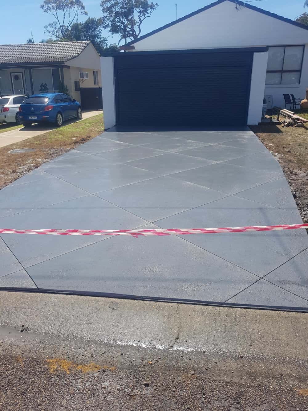 New Gray Concrete Driveway with A Black Garage Door — Coastcrete Concrete Specialist in Taylors Beach, NSW