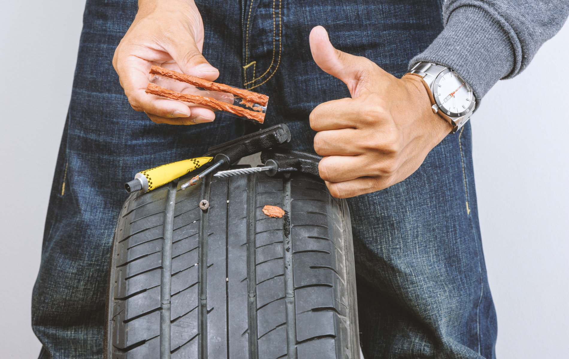 A man is fixing a tire with a screwdriver and giving a thumbs up.
