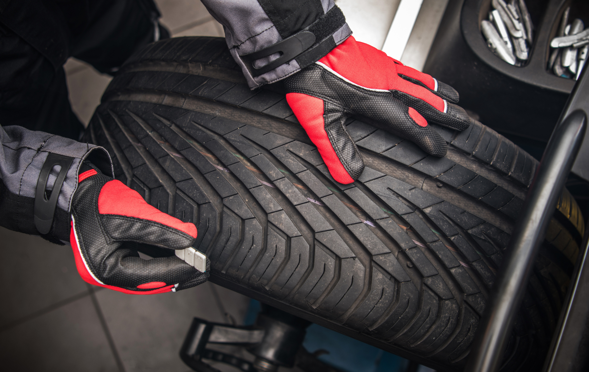 A person wearing red and black gloves is balancing a tire on a machine.
