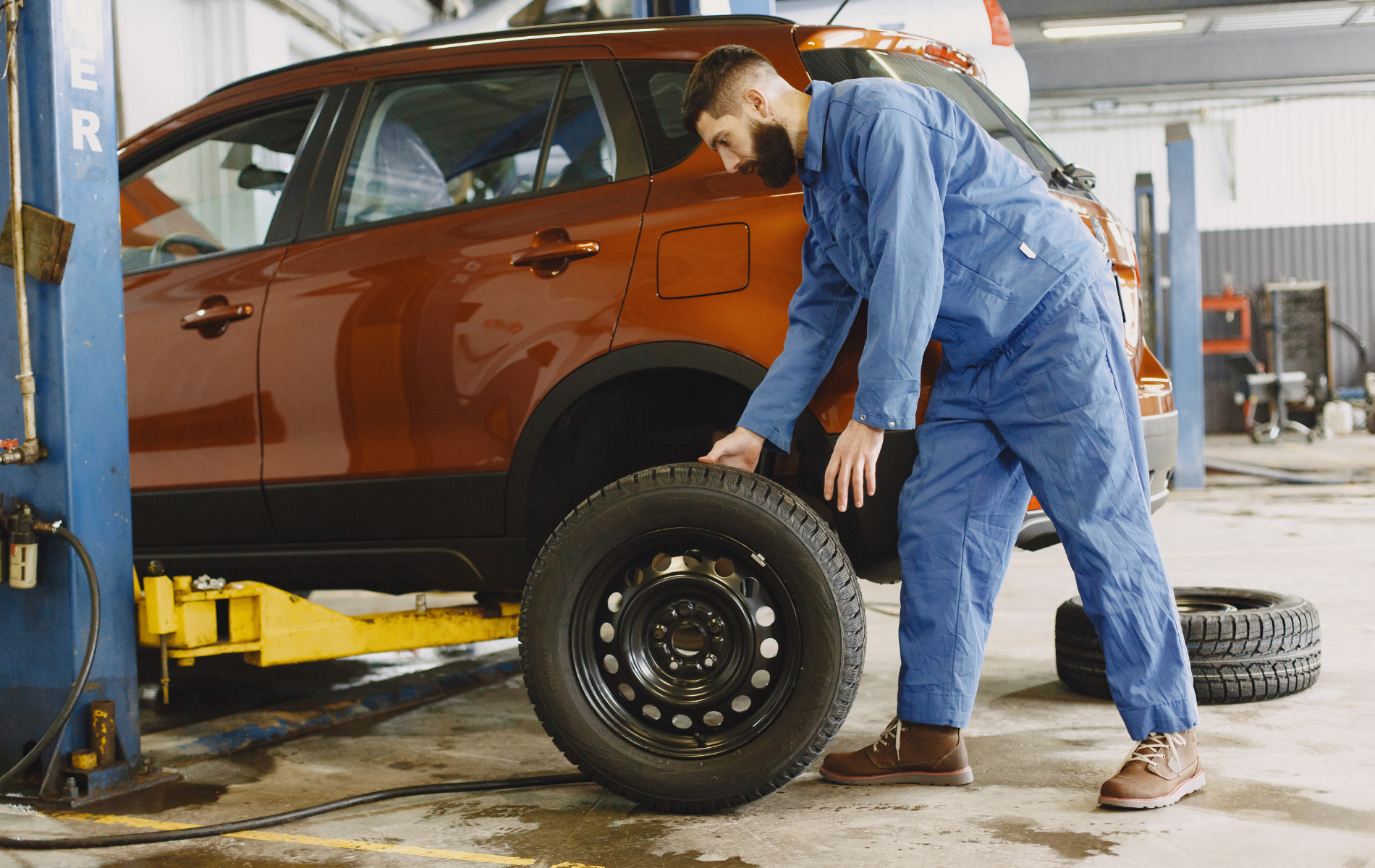 A man is changing a tire on a car in a garage.