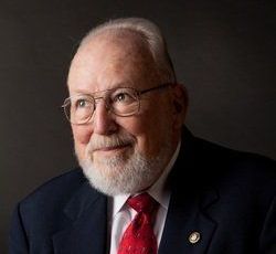 A man with a beard and glasses is wearing a suit and tie.