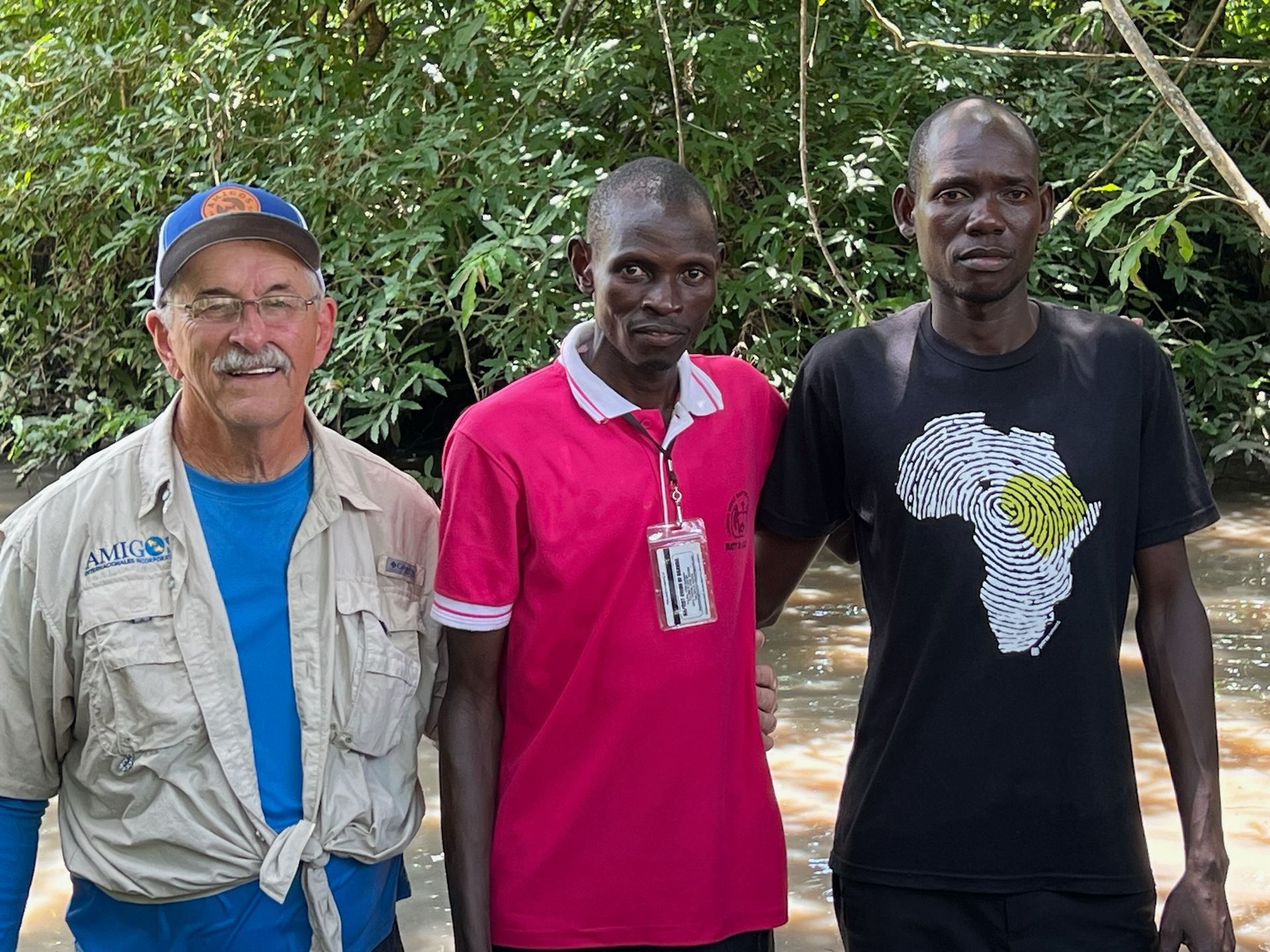 Three men are posing for a picture in front of trees.