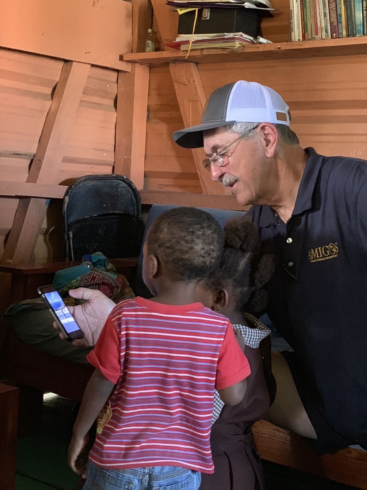 A man is talking to two children while holding a cell phone.