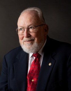 A man with a beard and glasses is wearing a suit and tie.
