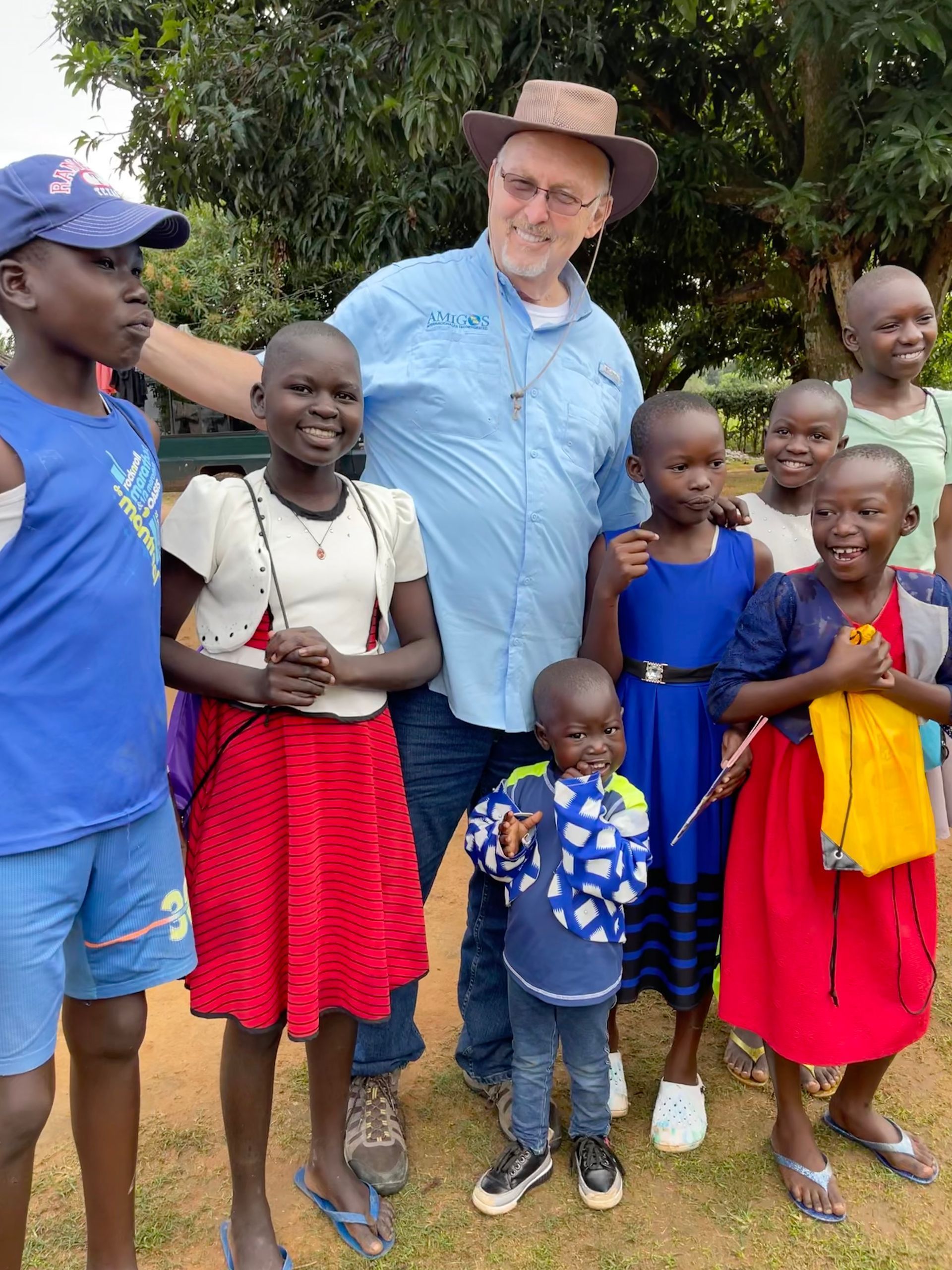 A man in a hat is standing next to a group of children.