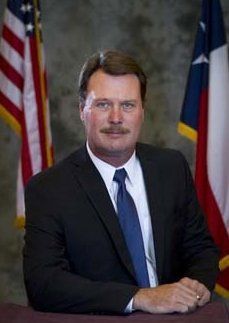 A man in a suit and tie is sitting in front of american flags.