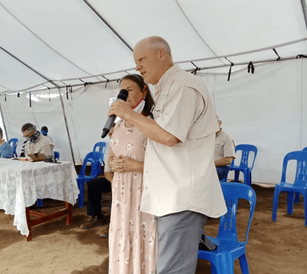 A man speaking into a microphone next to a woman in a pink dress