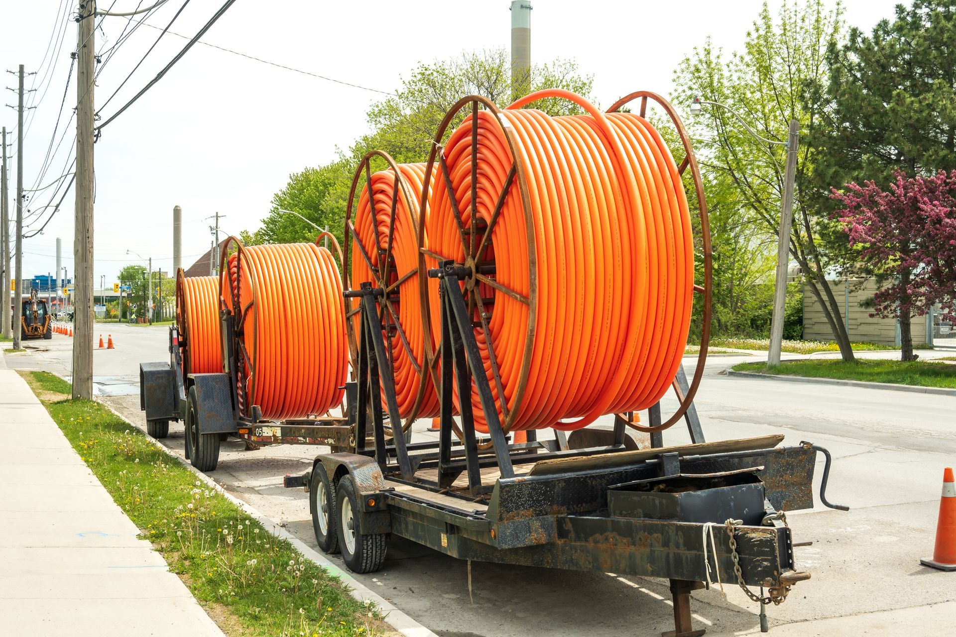 Three large orange spools of electrical wires are on a trailer on the side of the road.