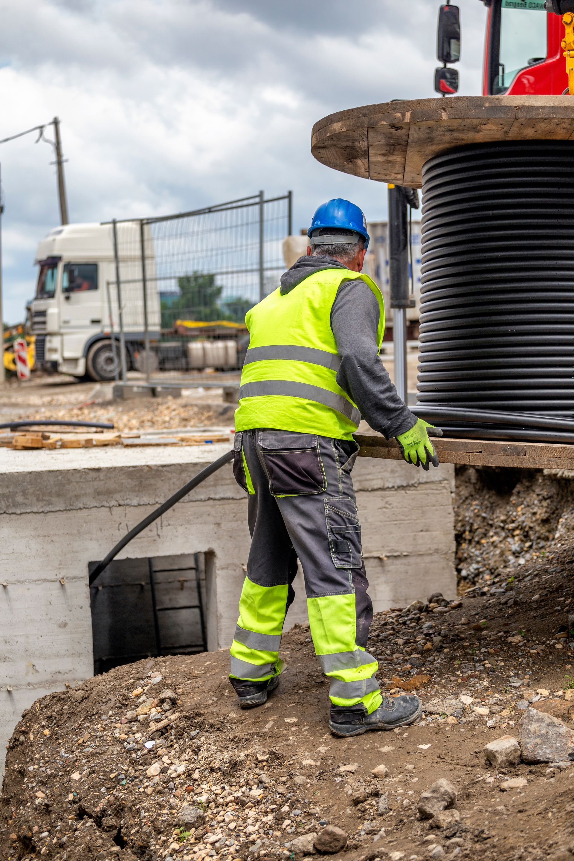 A construction worker is standing next to a large spool of cable.