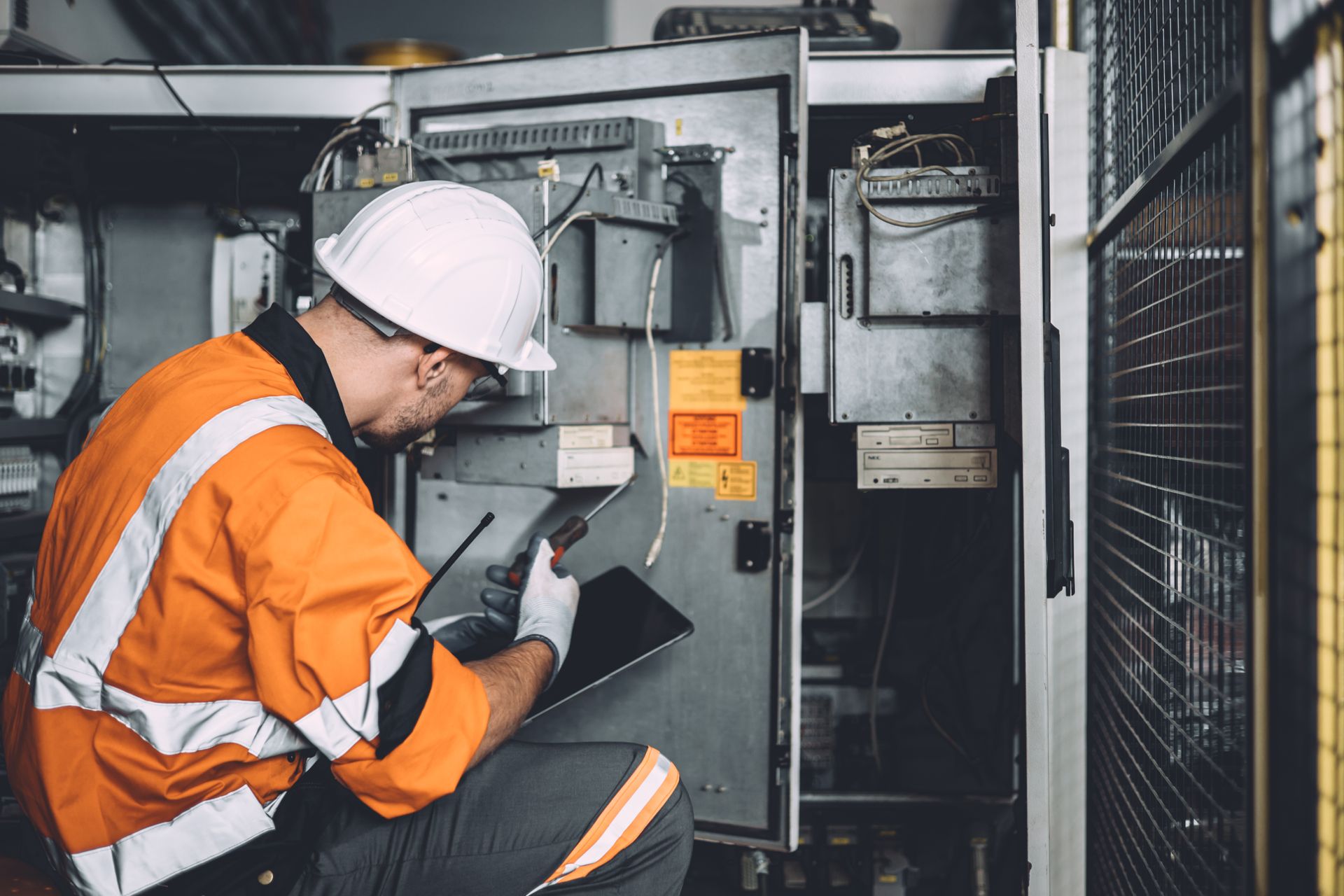 A man in a hard hat is kneeling down in front of an electrical box.