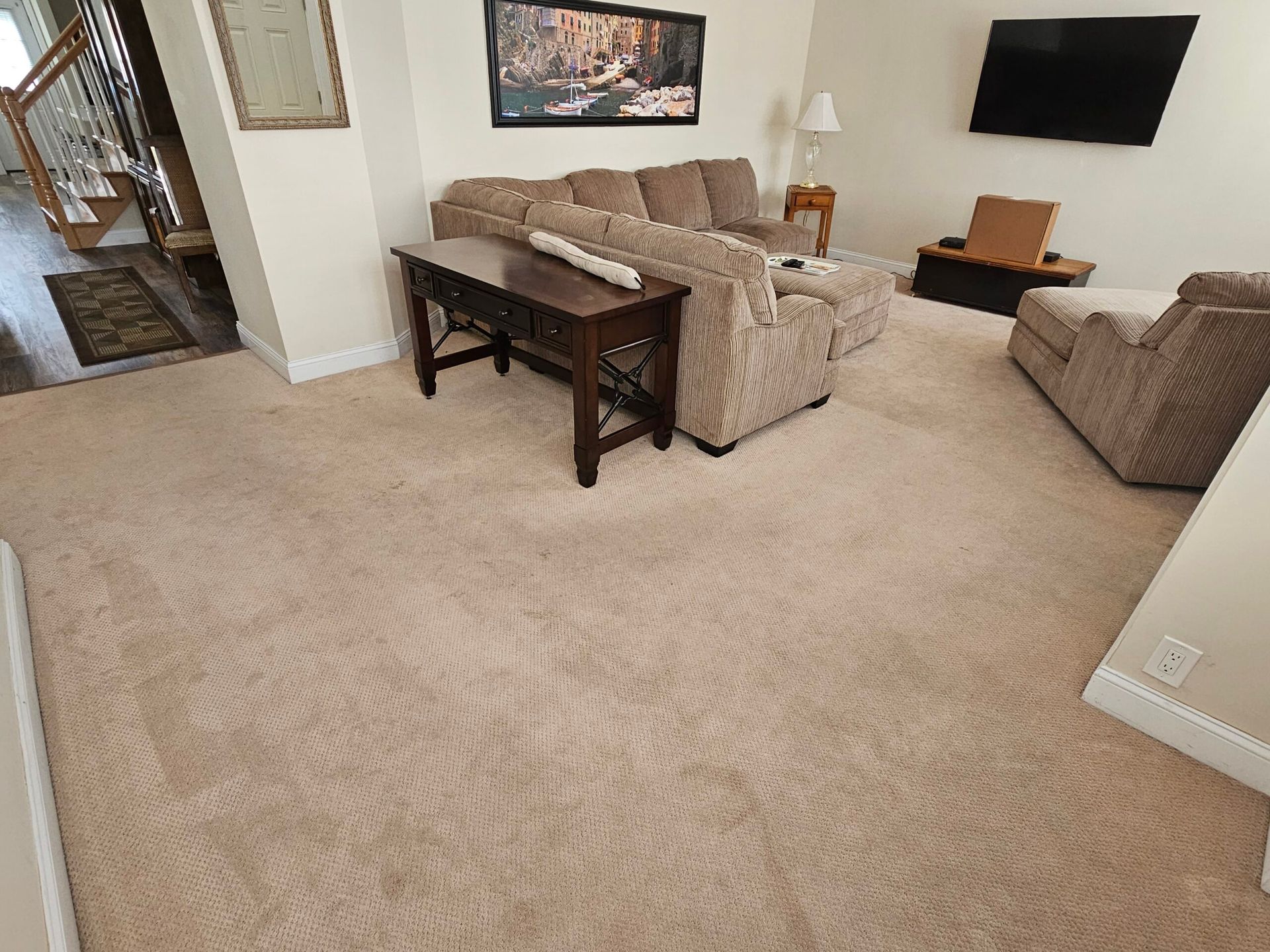 Beige carpeted living room with a sofa, TV, artwork, and a console table.
