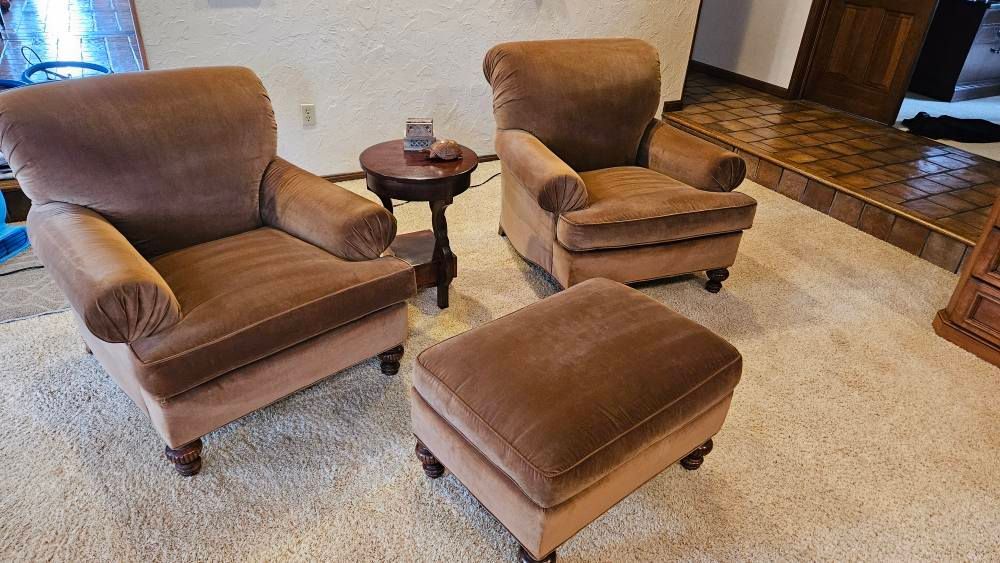 Two brown armchairs and an ottoman with a small side table, all in a room with carpet.