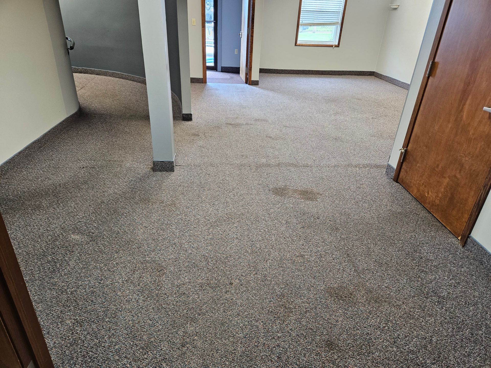 Room with speckled gray carpet, wood doors, and a window.