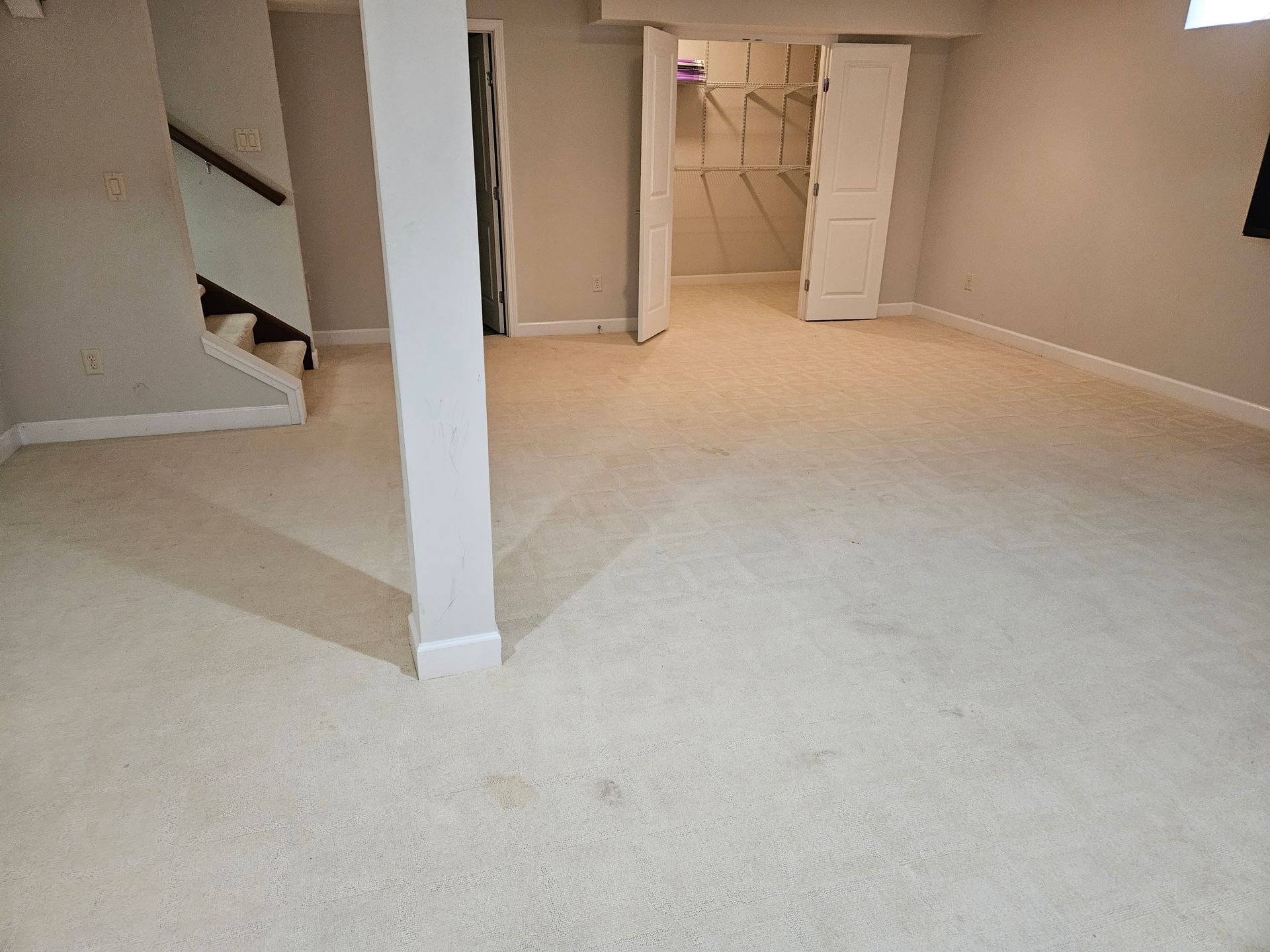 A room with light-colored carpet, a white support column, a closet, and a staircase.