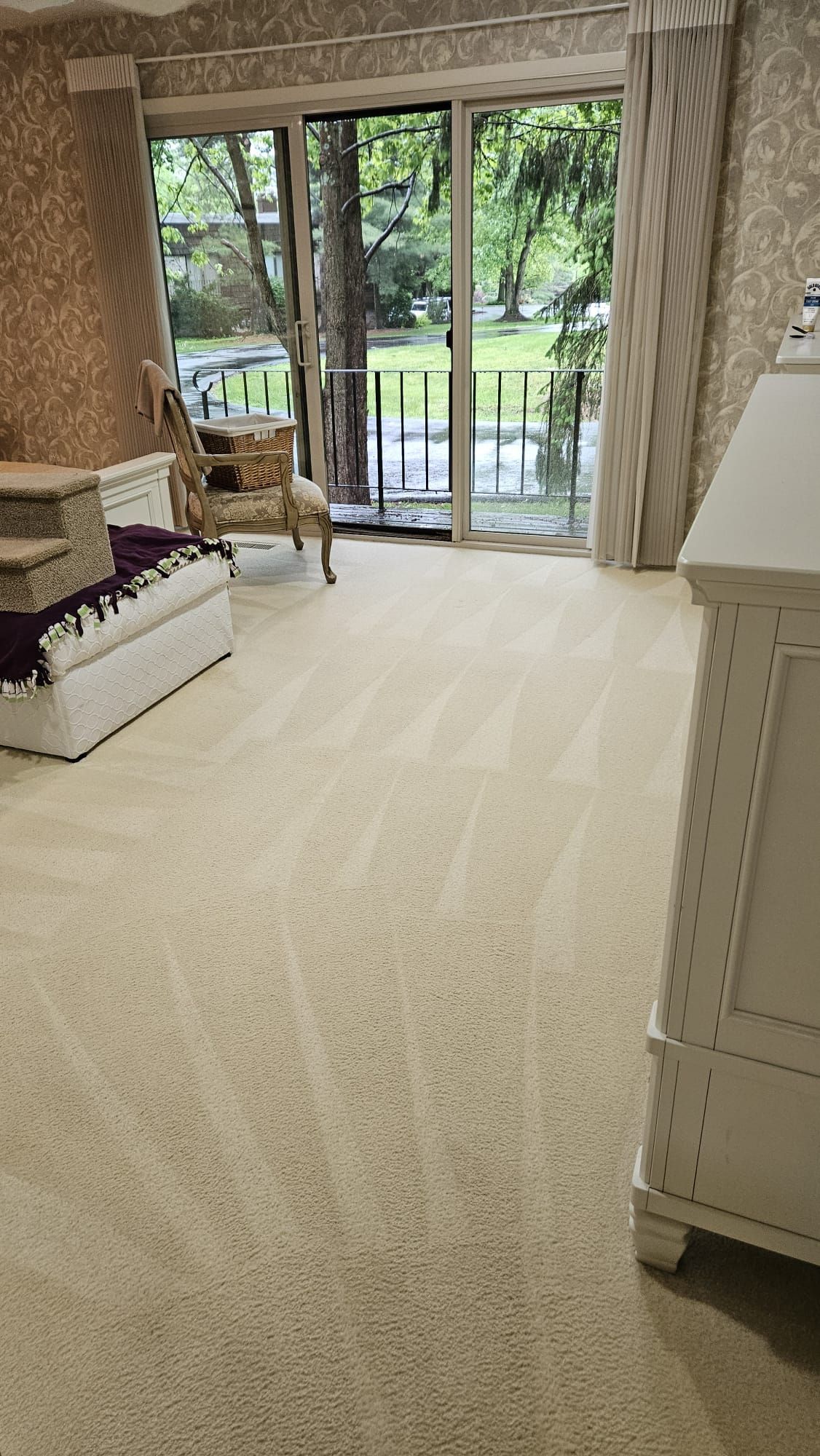 Beige carpeted room with open glass door to a balcony and a white dresser.