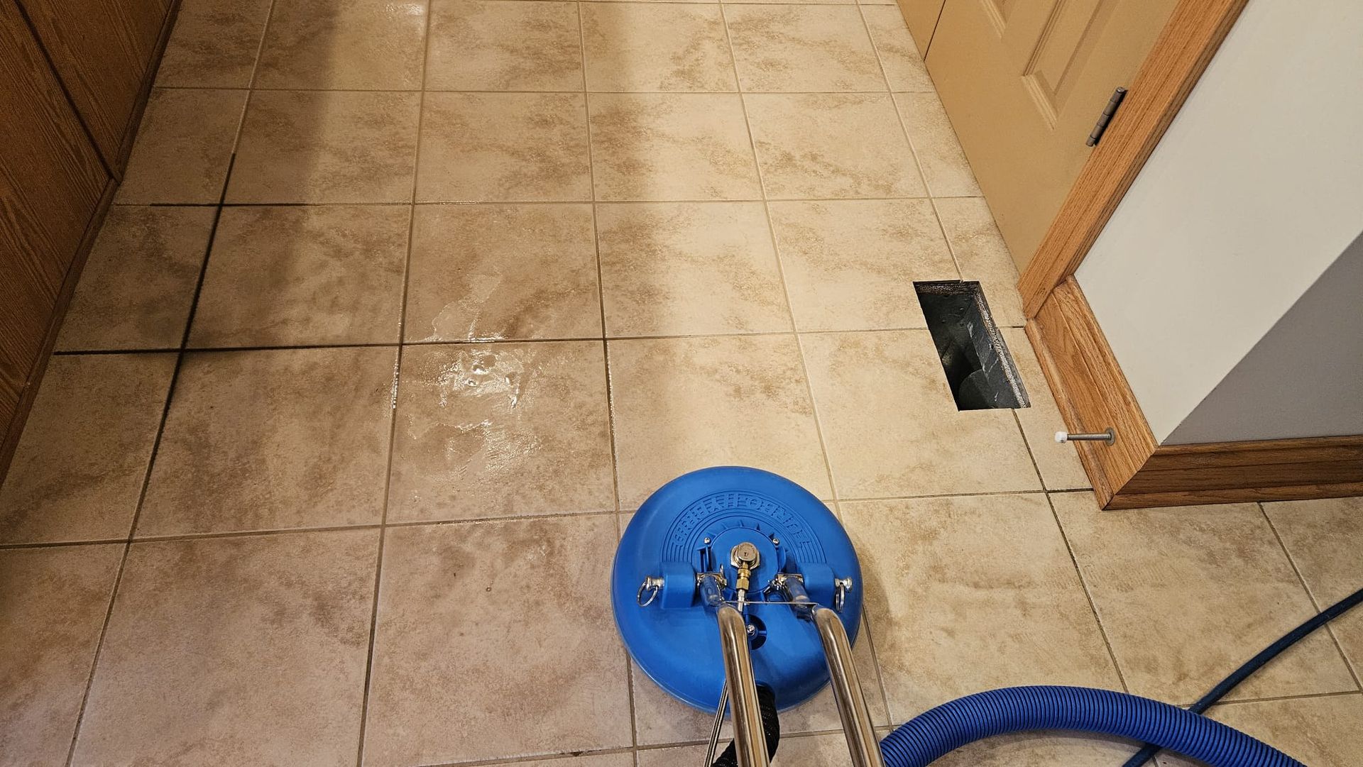 Blue floor cleaning machine on tan tile floor; near a vent and door.