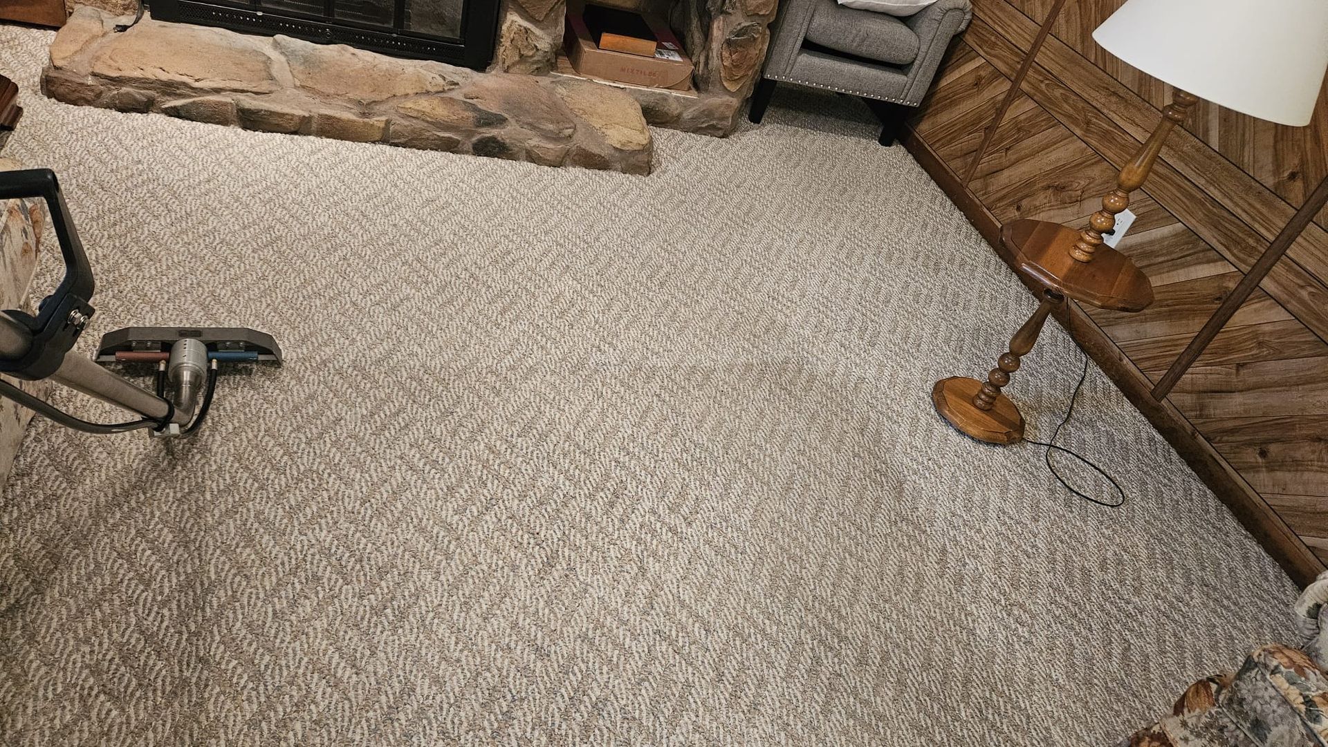 Vacuuming beige carpet in a living room with a fireplace and wooden wall paneling.