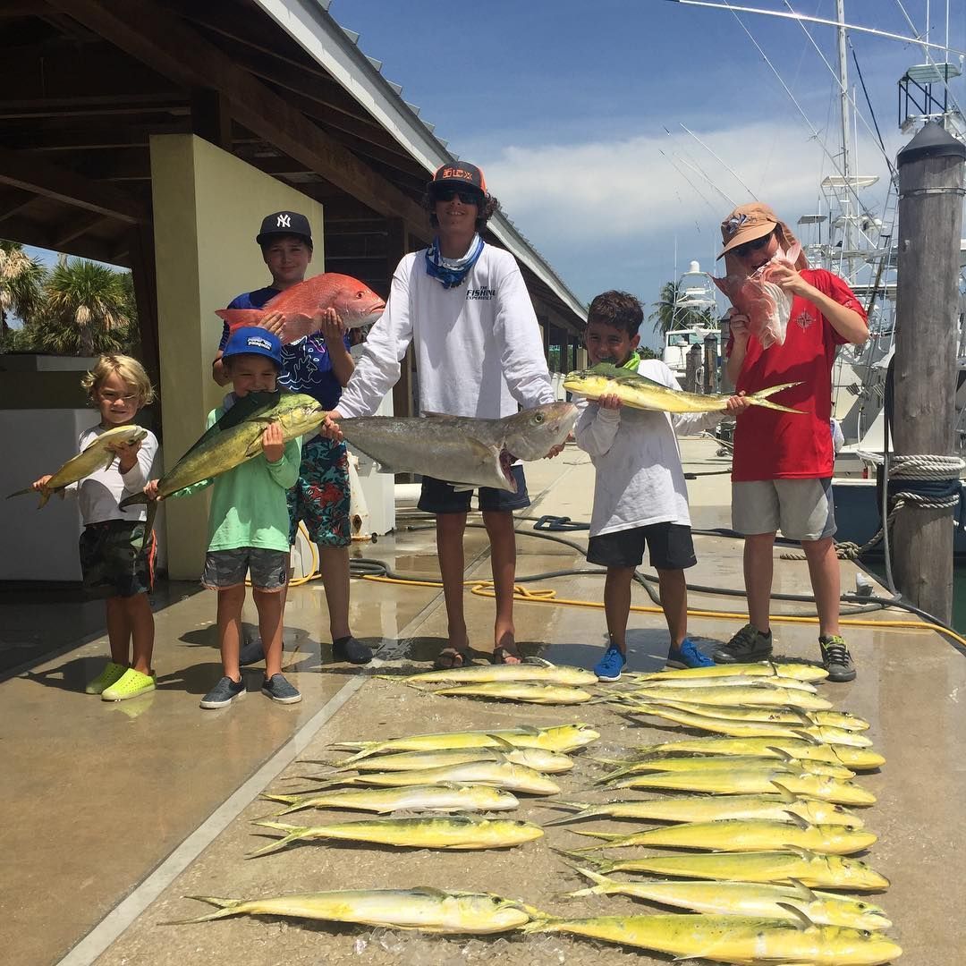 Group of people on a dock, holding fish. Several yellow fish lie on the ground.