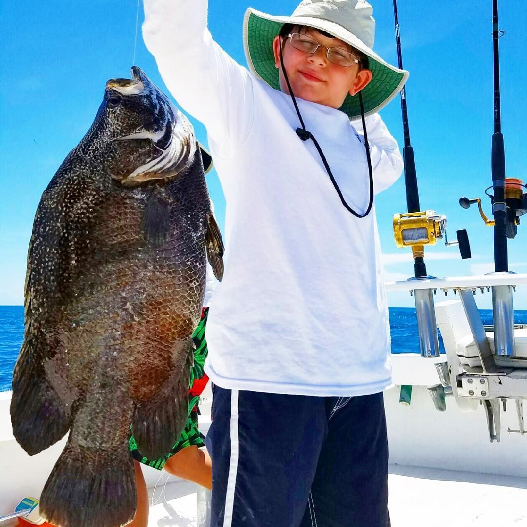 Boy holding a large fish up in triumph on a boat, blue sky backdrop.