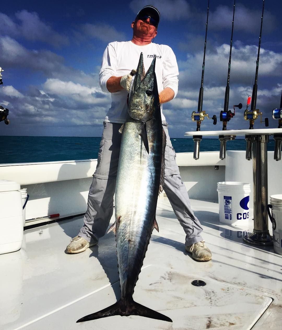 Man on boat holds up large fish with blue water background.