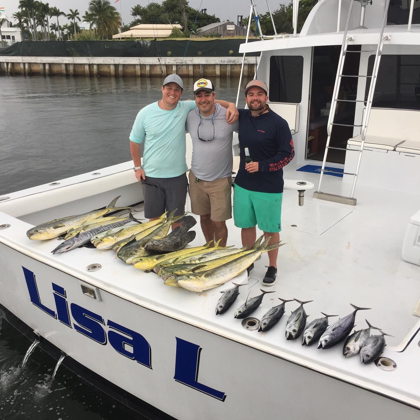 Three men stand on a boat, smiling, with a display of caught fish: mahi-mahi and tuna. 