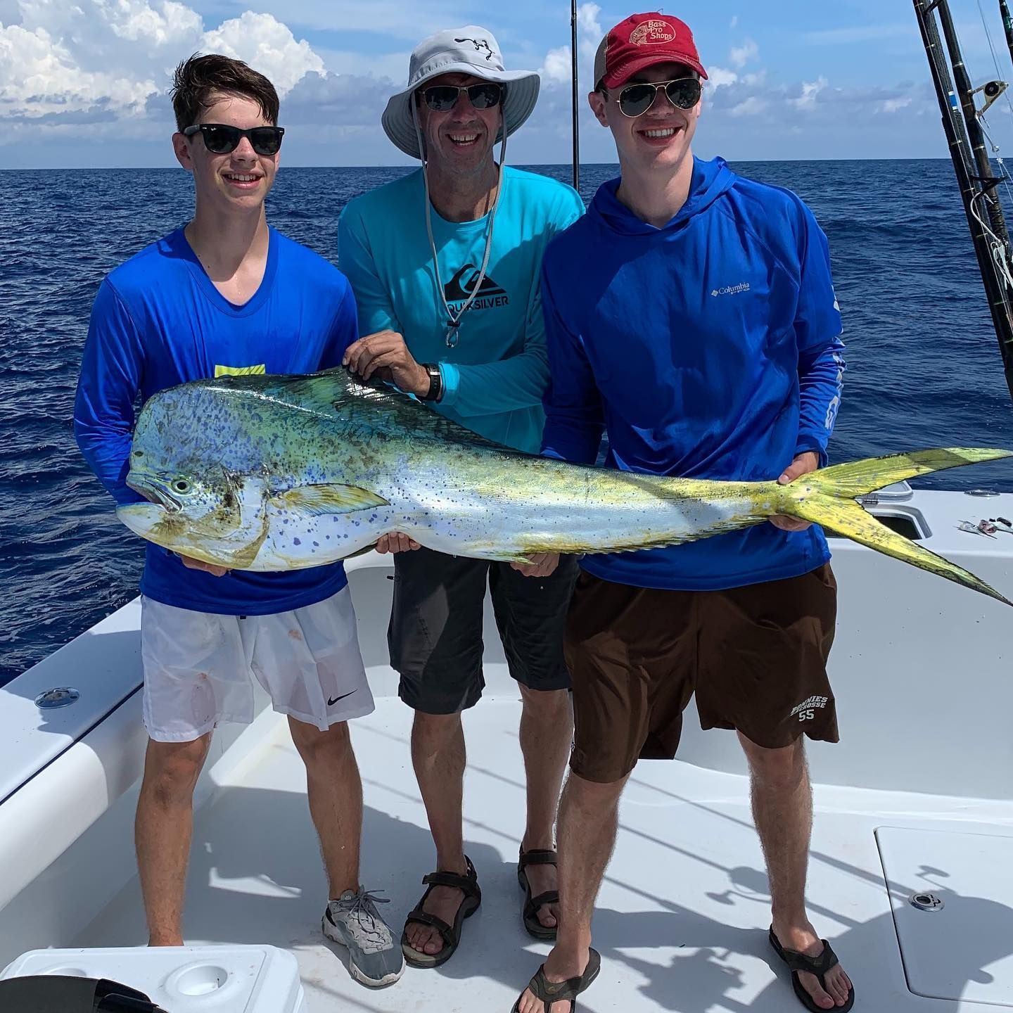 Three people on a boat holding a large, colorful mahi-mahi fish. Blue water and sky.