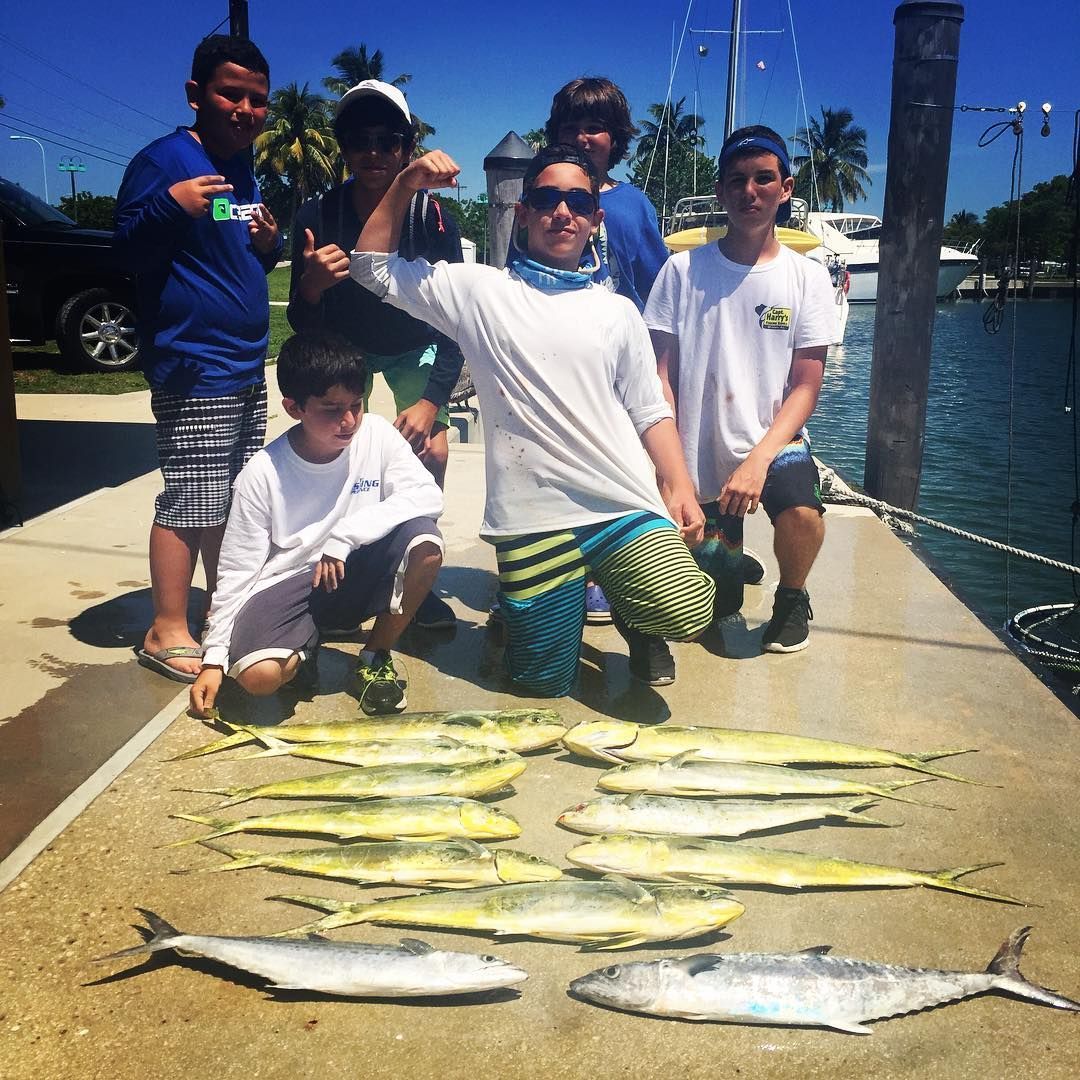 Group of people pose with a catch of fish on a dock in sunlight.