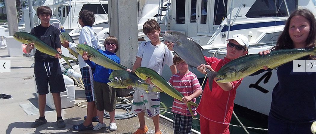 A group of people holding up fish they caught. They are standing near a boat.