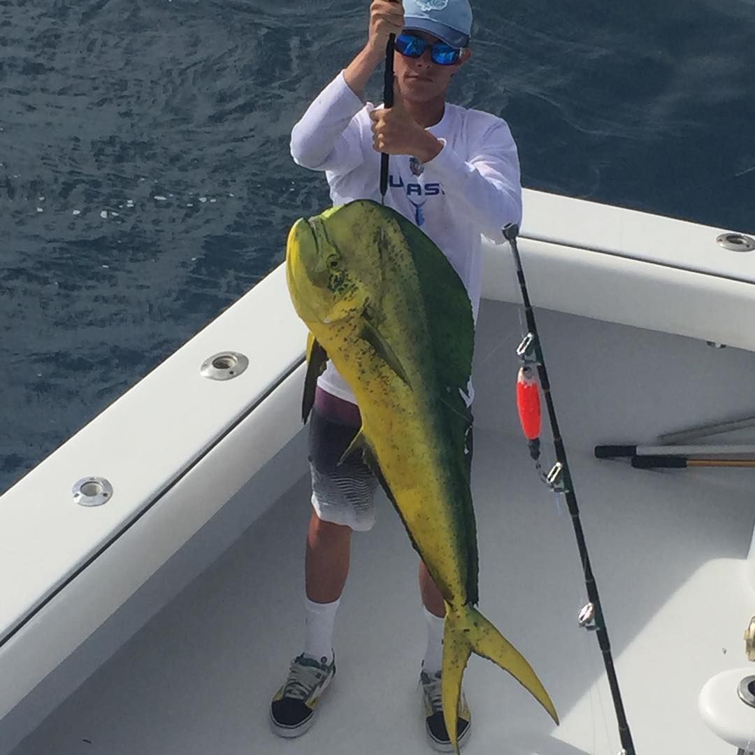 Man on a boat holding a large, yellow and green mahi-mahi fish he caught.