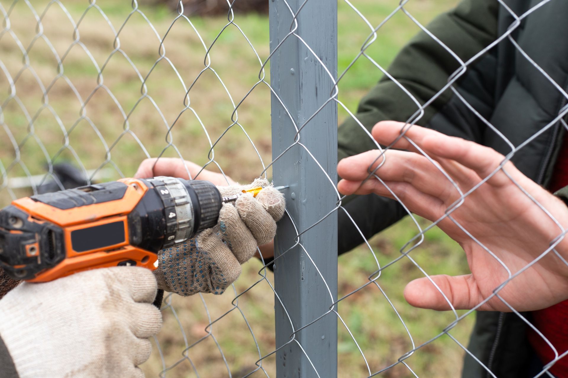 A man is using an electric drill to install a chain-link fence.